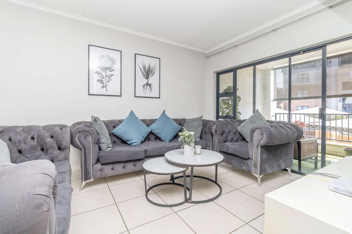 A bright living room featuring neutral tiled flooring and large sliding glass doors that provide access to an outdoor balcony area.