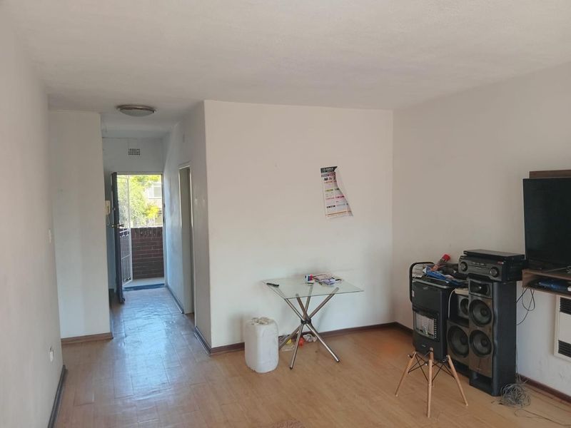 A living room area featuring laminate flooring and access to an exterior balcony through a security gate.