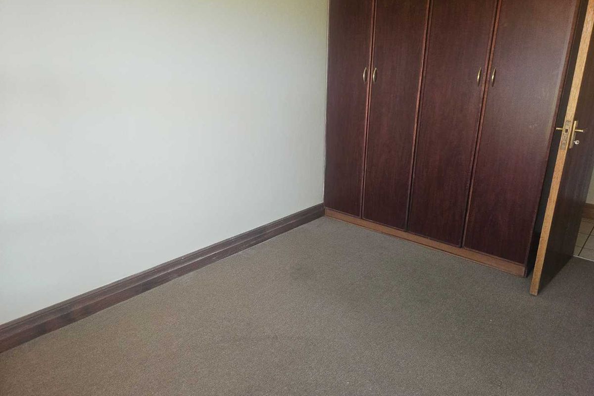 An empty bedroom featuring built-in wooden cupboards and carpeted flooring, offering a blank canvas for personalization.