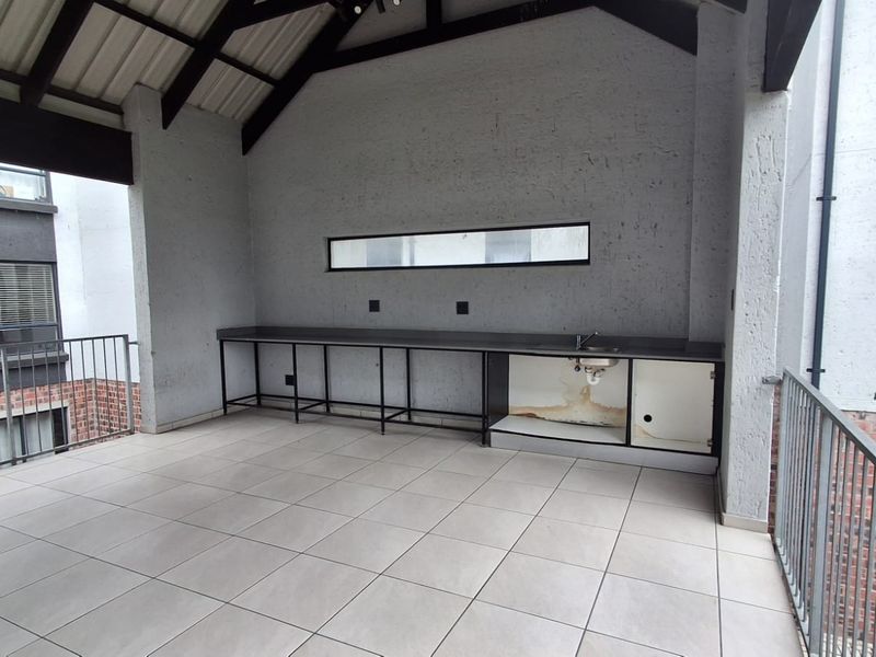 Covered balcony featuring tiled flooring, exposed roof trusses, and a built-in counter with a sink, offering a versatile outdoor space.