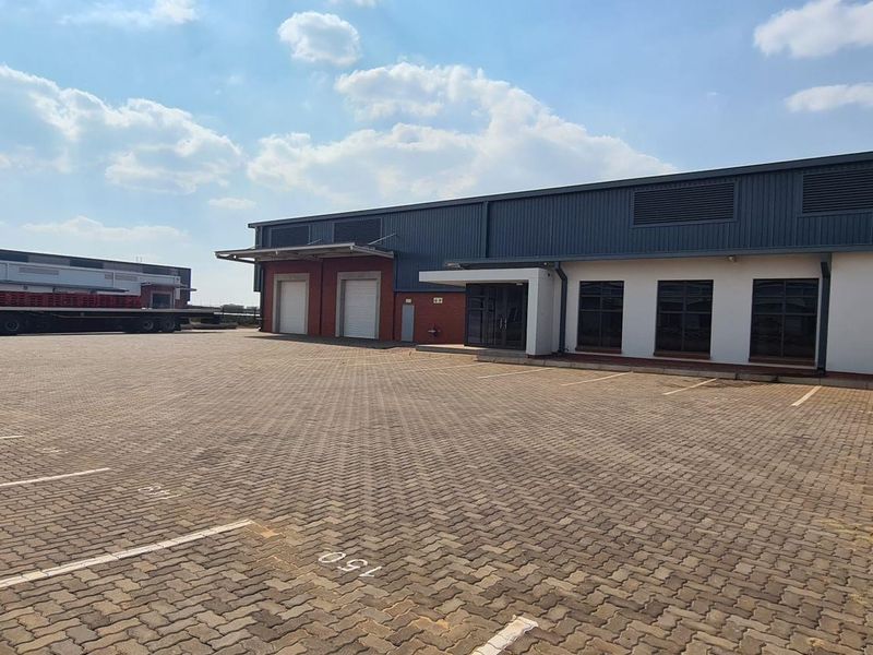 A wide-angle view of an industrial property featuring a large paved parking area, loading bays, and a modern warehouse facade.