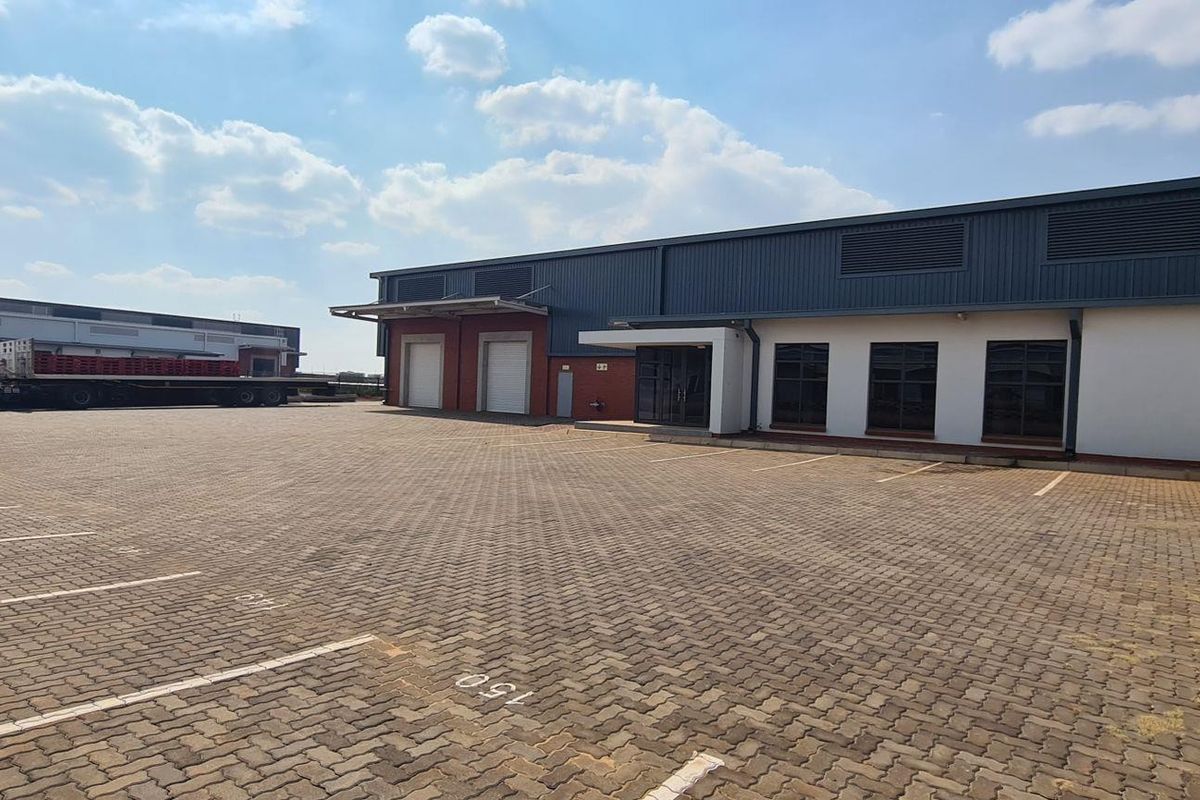 A wide-angle view of an industrial property featuring a large paved parking area, loading bays, and a modern warehouse facade.
