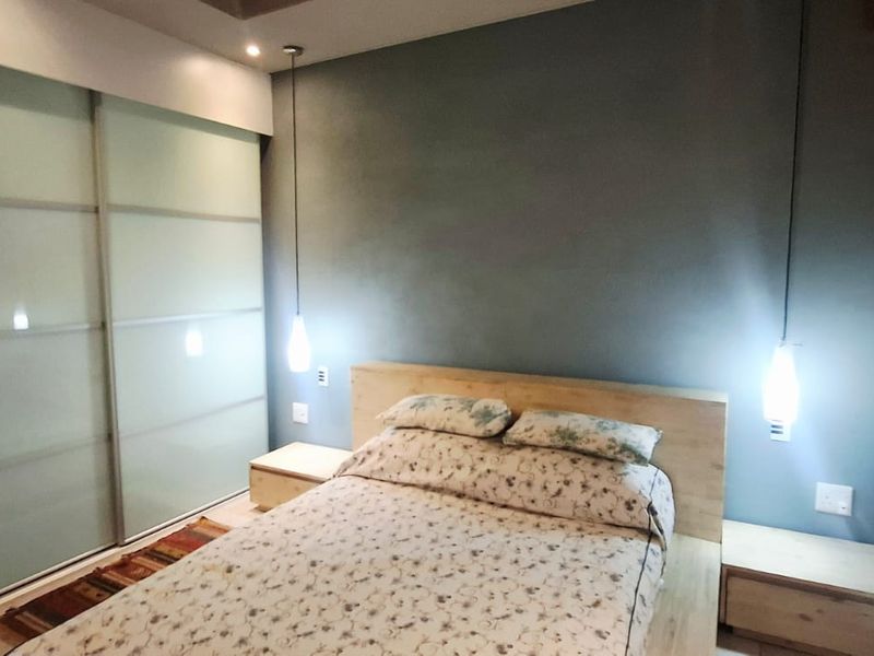 A modern bedroom featuring a large built-in sliding door wardrobe, stylish pendant lighting, and neutral tiled flooring.