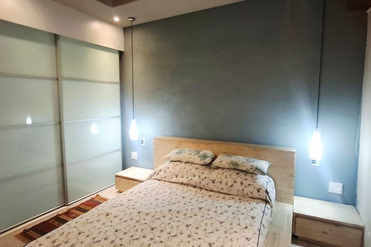 A modern bedroom featuring a large built-in sliding door wardrobe, stylish pendant lighting, and neutral tiled flooring.