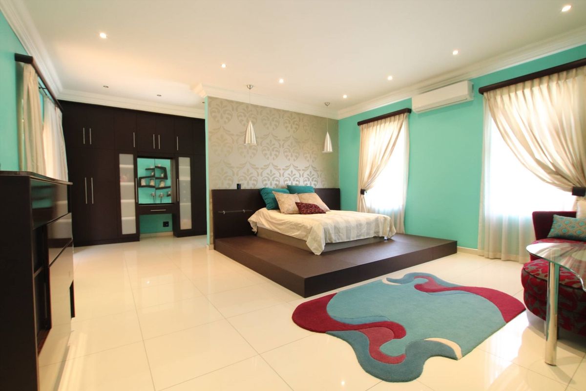 Spacious bedroom featuring a raised platform bed area, built-in dark wood cabinetry, recessed ceiling lighting, and a wall-mounted air conditioning unit.