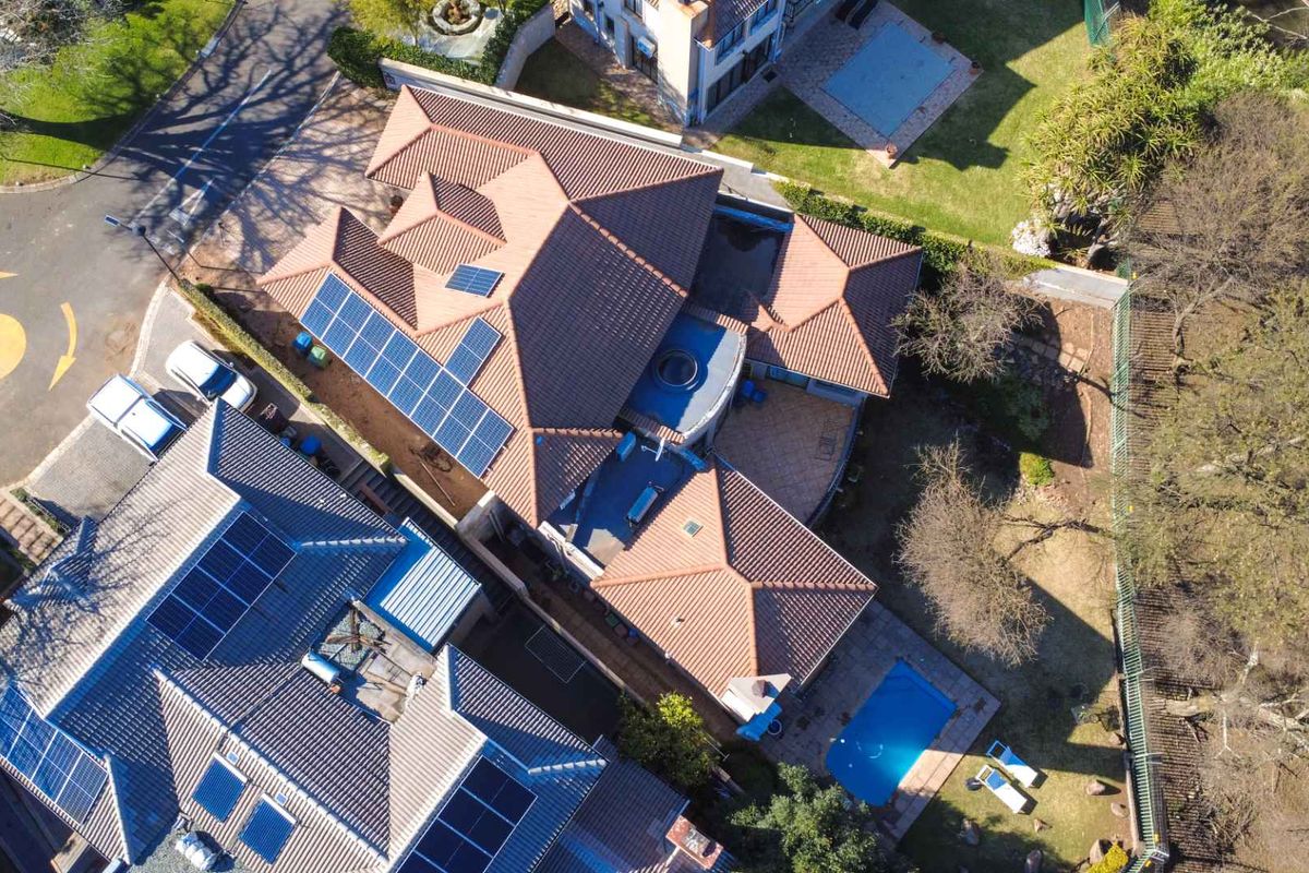 Aerial view of the property showcasing the tiled roof with solar panels, swimming pool, and surrounding garden area.