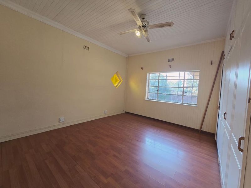 A spacious, empty bedroom featuring laminate flooring, a ceiling fan, and built-in cupboards, offering a blank canvas for personalization.
