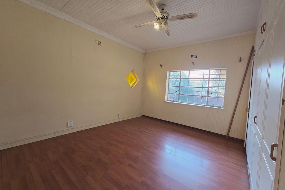 A spacious, empty bedroom featuring laminate flooring, a ceiling fan, and built-in cupboards, offering a blank canvas for personalization.