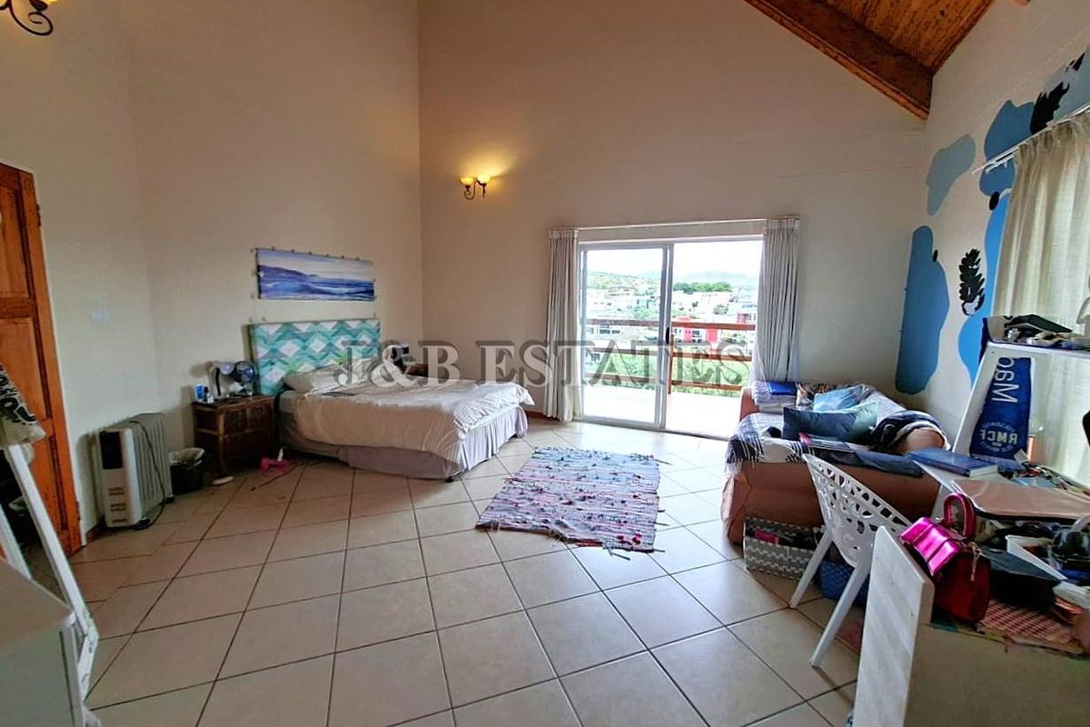 Spacious bedroom featuring high vaulted timber ceilings, tiled flooring, and sliding glass doors leading to a private balcony with scenic views.