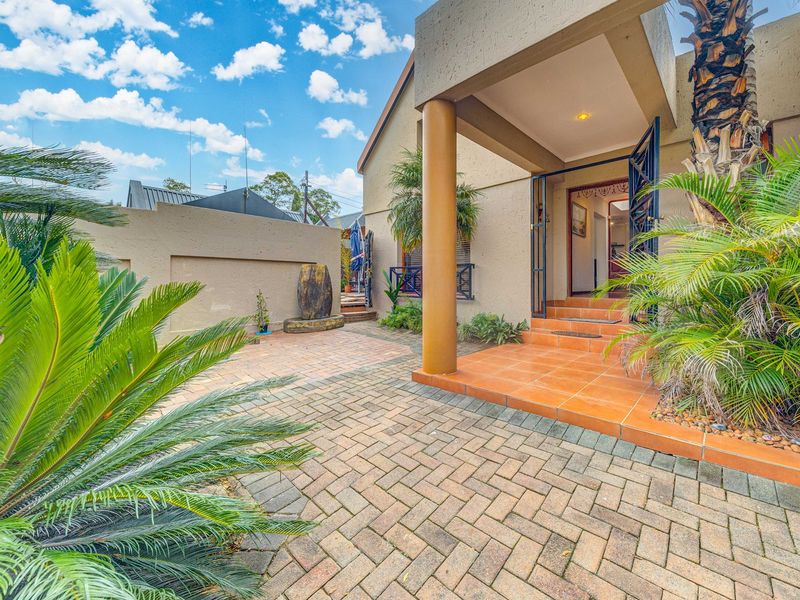 A well-maintained front entrance featuring a paved driveway, covered porch with a structural pillar, and secure gated access to the home.