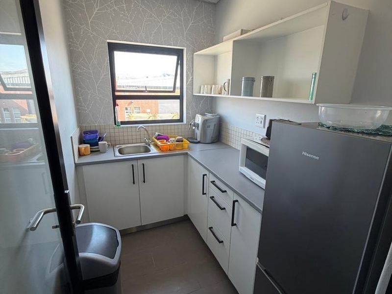 Compact scullery area featuring built-in cabinetry, laminate countertops, a stainless steel sink, and tiled flooring, providing functional workspace and storage.