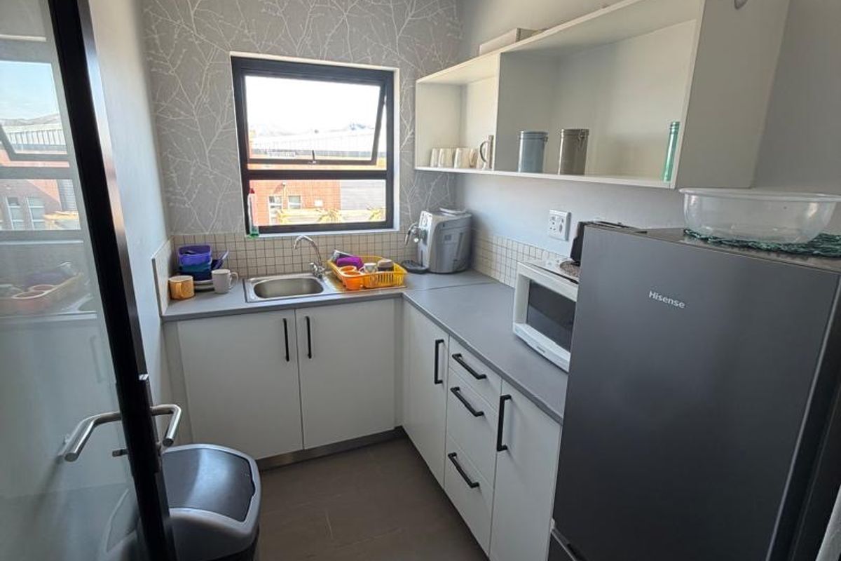 Compact scullery area featuring built-in cabinetry, laminate countertops, a stainless steel sink, and tiled flooring, providing functional workspace and storage.