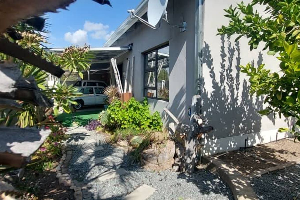 A view of the exterior rear of the townhouse, featuring a landscaped garden path, gravel area, and a covered patio space.