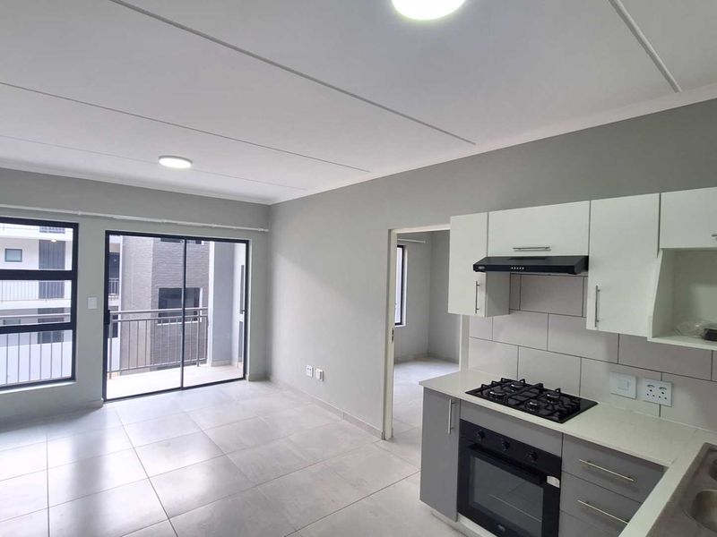 Modern open-plan living area featuring a contemporary kitchen with built-in appliances, tiled flooring, and direct access to a private balcony.
