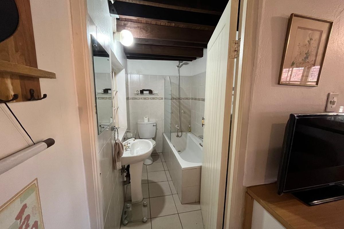 A compact bathroom featuring a pedestal sink, toilet, and a shower-over-bath combination with exposed timber ceiling beams.