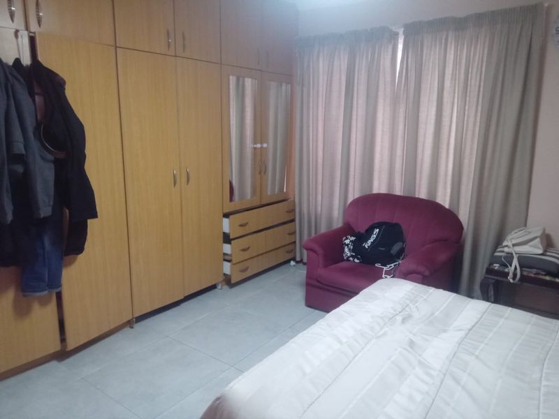 A bedroom featuring built-in wooden cupboards with integrated mirror and tiled flooring.