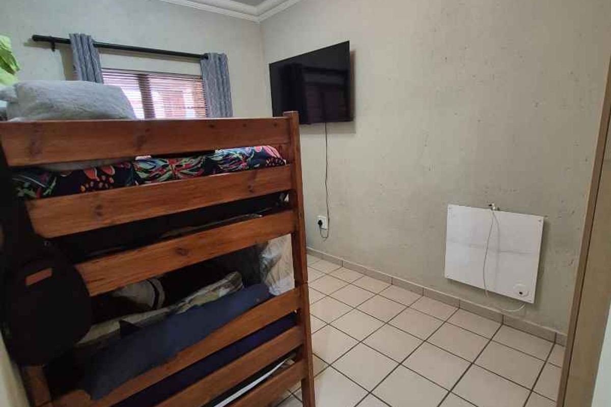 A compact bedroom featuring tiled flooring, crown molding, and a wall-mounted electric heater.