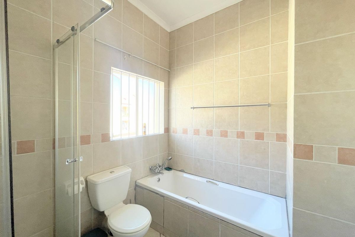 A functional bathroom featuring a built-in bathtub, glass shower screen, and a standard toilet with neutral wall tiling.