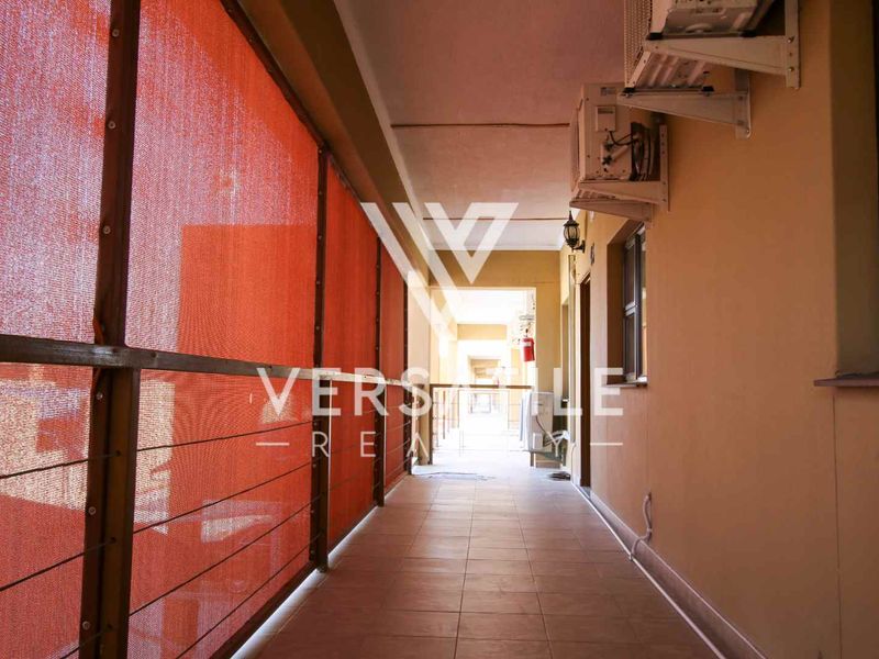 A covered balcony or walkway featuring tiled flooring, an air conditioning unit, and a red privacy screen, providing a functional outdoor transition space.