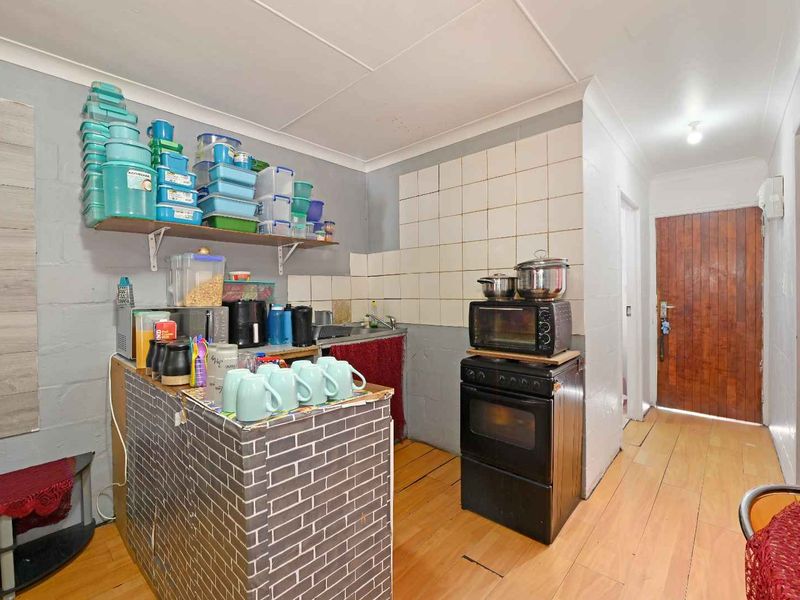 A compact kitchen area featuring a built-in oven, sink, tiled splashback, and laminate flooring, requiring cosmetic updates to improve the overall finish.