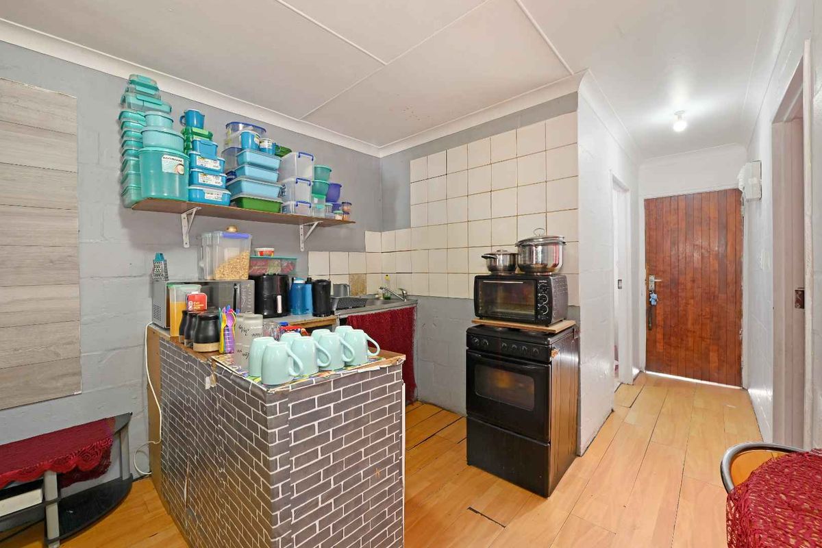 A compact kitchen area featuring a built-in oven, sink, tiled splashback, and laminate flooring, requiring cosmetic updates to improve the overall finish.