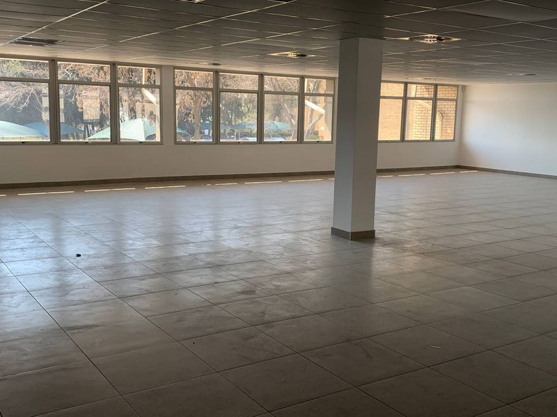A spacious, open-plan industrial office area featuring large windows, tiled flooring, and a suspended ceiling with recessed lighting.