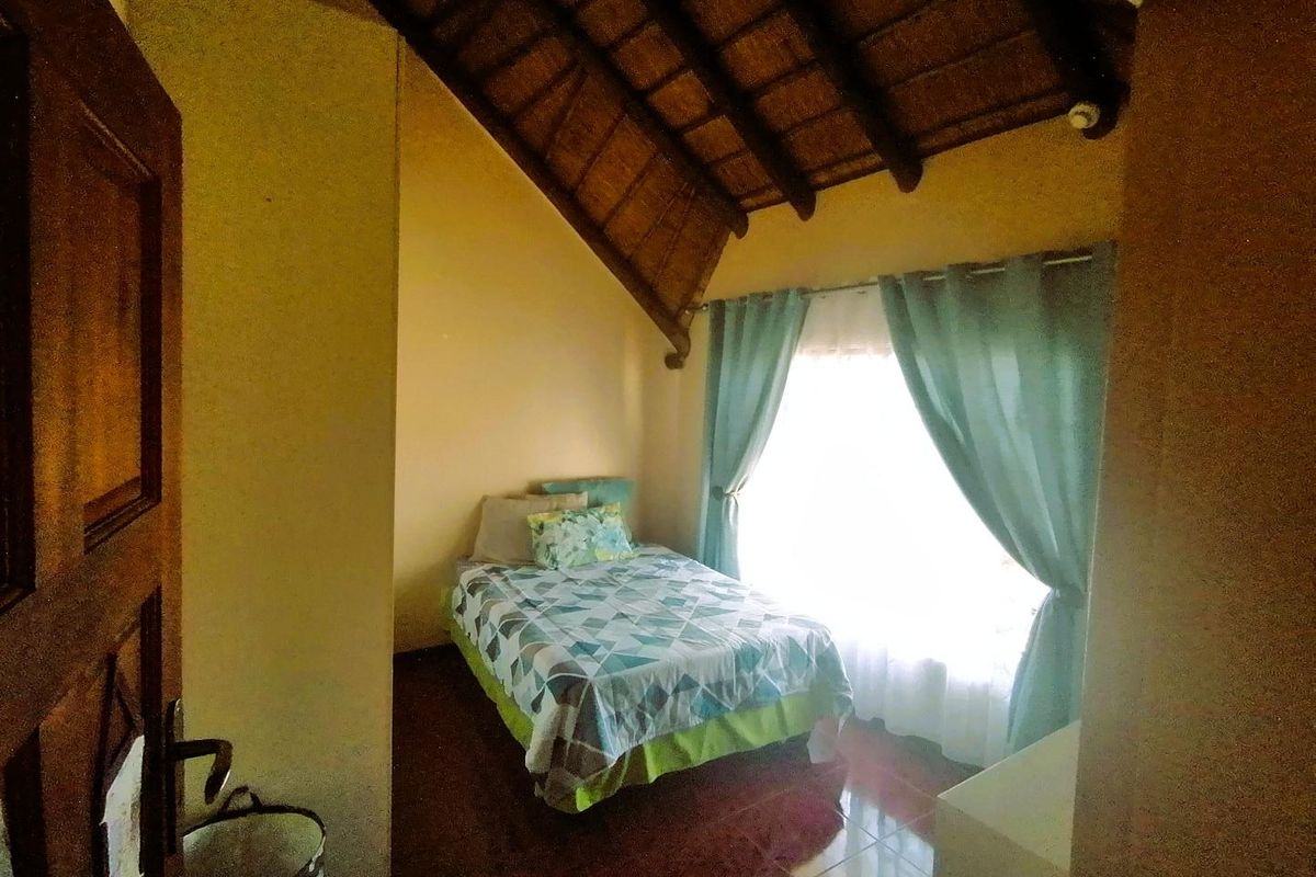 A cozy bedroom featuring a high vaulted thatched ceiling, tiled flooring, and natural light through a window with curtains.