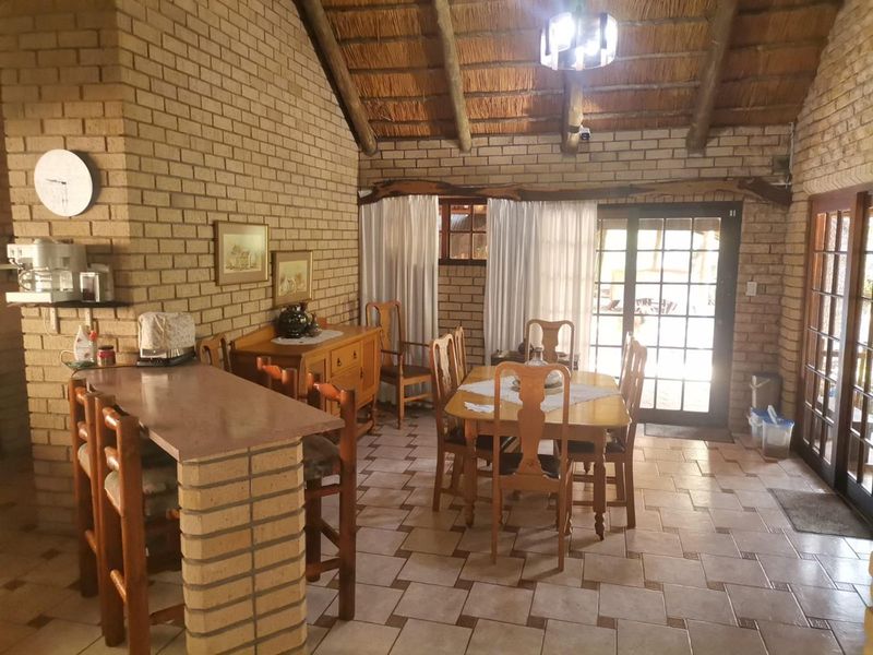 Open-plan living and dining area featuring exposed brick walls, a high thatched ceiling with timber beams, and direct access to the outdoors via french doors.