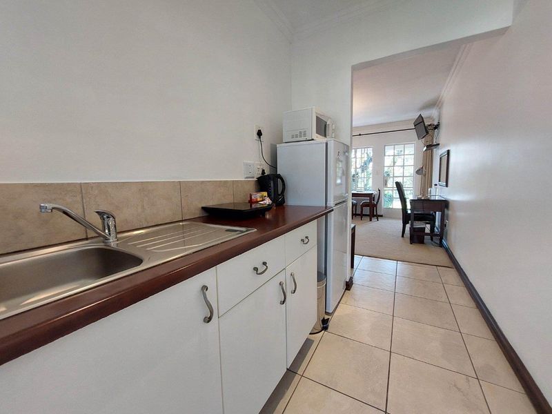 A compact kitchen area featuring white cabinetry, a stainless steel sink, and tiled flooring, leading into an adjacent living space.