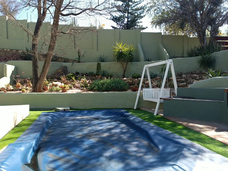 Outdoor pool area featuring a covered swimming pool, tiered retaining walls with landscaping, and a built-in bench seating area.