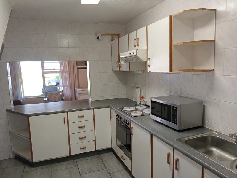 A functional kitchen featuring built-in cabinetry, laminate countertops, a stainless steel sink, and integrated cooking appliances with a tiled splashback.