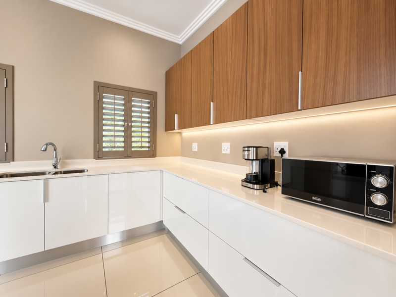 Modern kitchen featuring high-gloss white lower cabinets, wood-finish upper cabinetry, stone countertops, under-cabinet lighting, and elegant plantation shutters.
