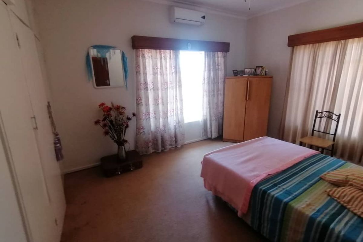 A bedroom featuring built-in cupboards, a ceiling fan, and a wall-mounted air conditioning unit.