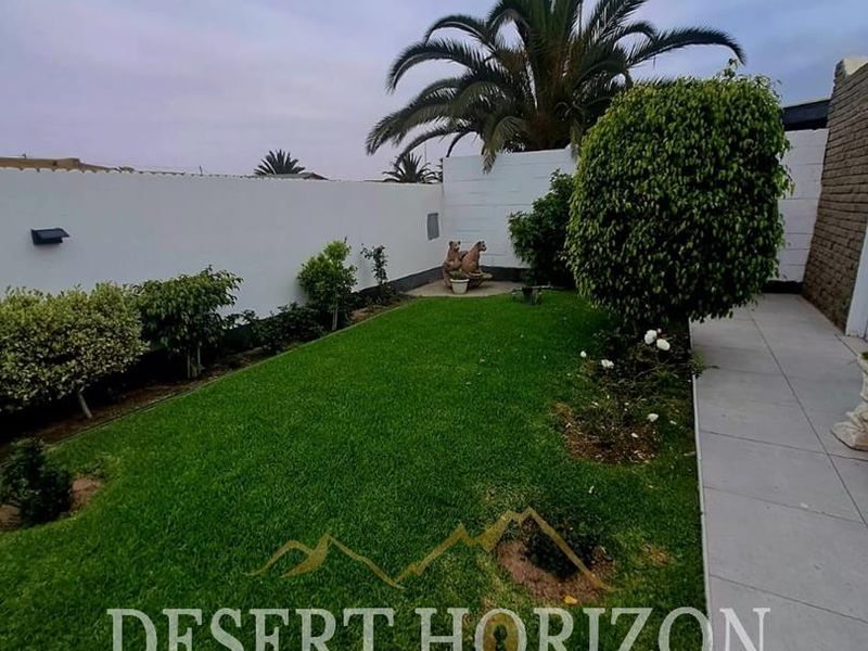 A well-maintained private garden featuring a lush green lawn, paved walkway, and perimeter boundary walls.