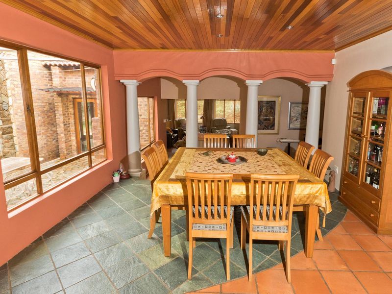 Spacious dining area featuring a warm timber ceiling, decorative columns, and a combination of slate and terracotta tile flooring with large windows.