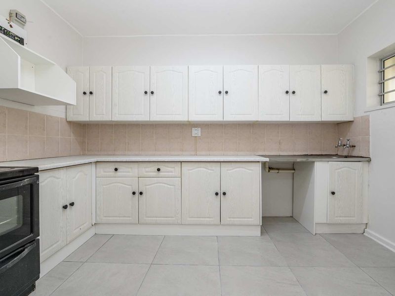 A functional kitchen featuring white built-in cabinetry, tiled backsplash, tiled flooring, and a stainless steel sink with security bars on the window.