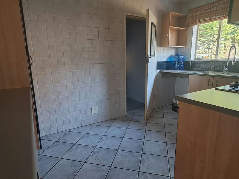 A functional kitchen featuring built-in cabinetry, a gas hob, tiled splashbacks, and tiled flooring, offering a practical layout ready for modernization.