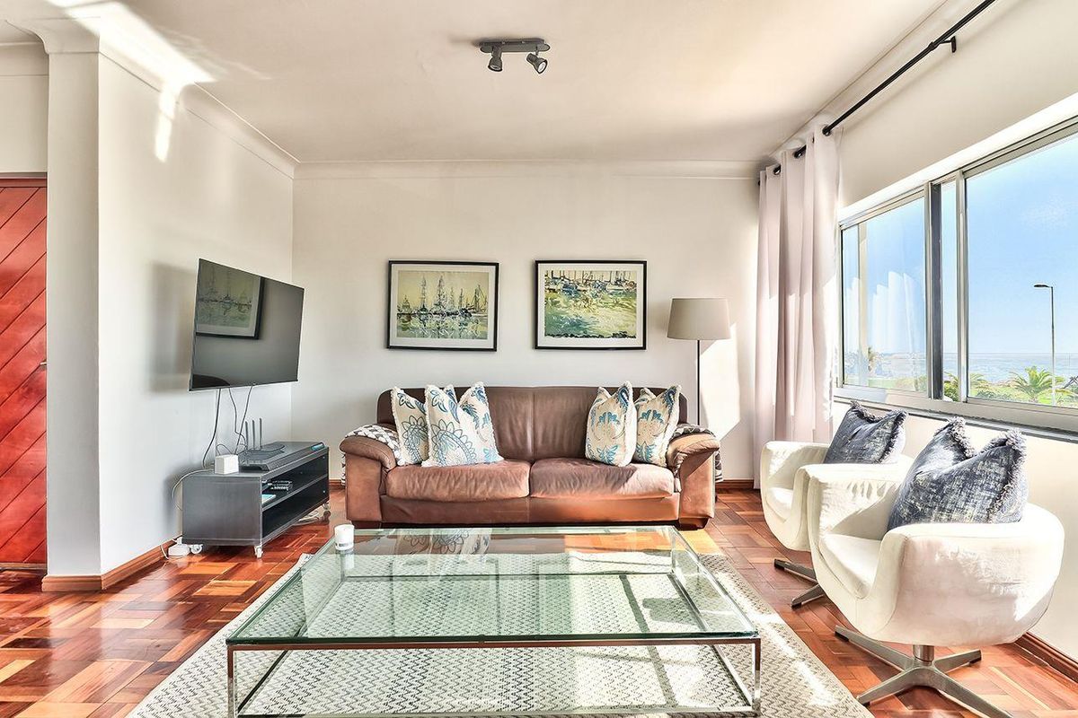 A bright living room featuring polished parquet flooring, large windows with natural light, and modern track lighting.