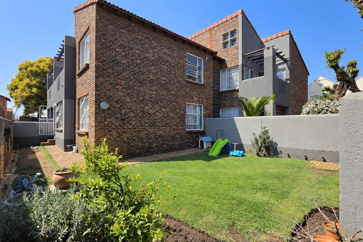 Rear view of a double-story townhouse featuring a face brick facade, private garden, paved walkway, and upper-level balcony with a pergola.