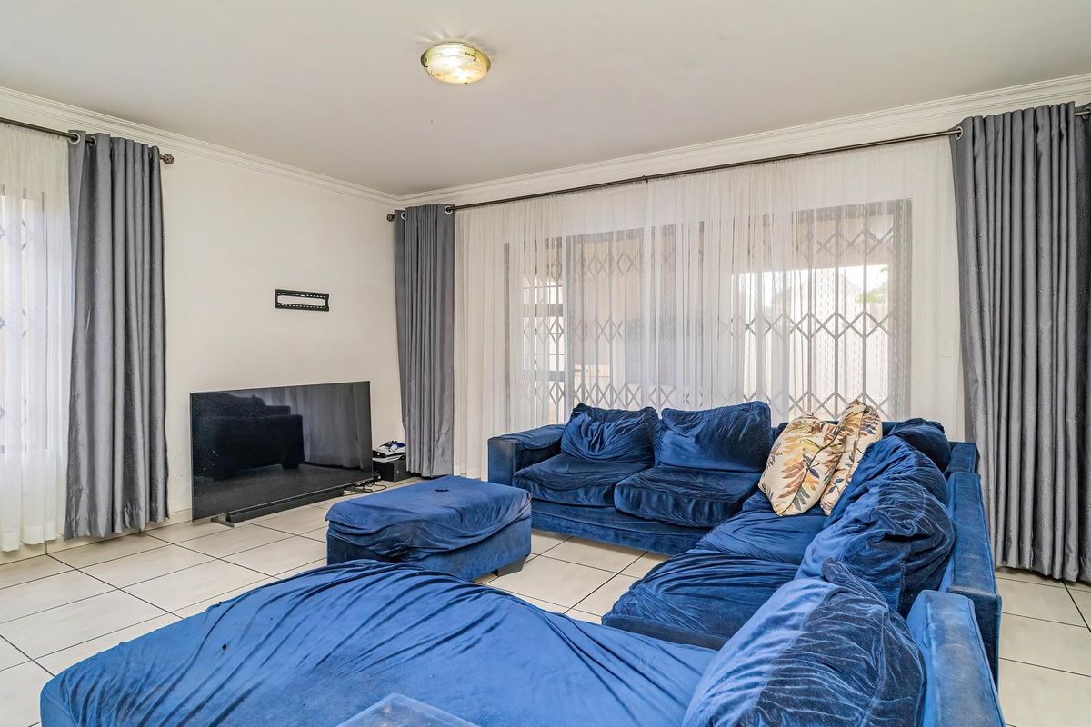 Spacious living room featuring neutral tiled flooring, large sliding glass doors with security gates, and classic ceiling cornicing.