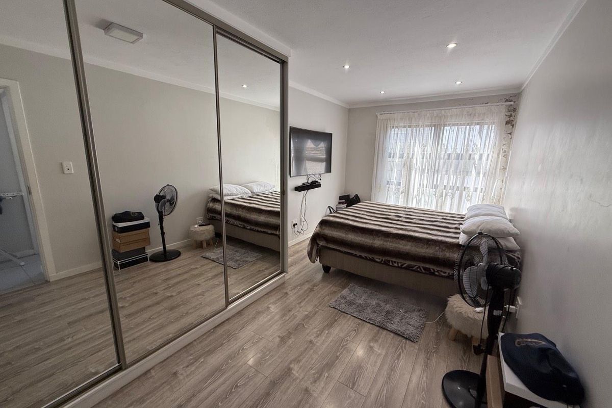 A well-maintained bedroom featuring modern wood-look laminate flooring, recessed ceiling lighting, and large floor-to-ceiling mirrored sliding wardrobe doors.