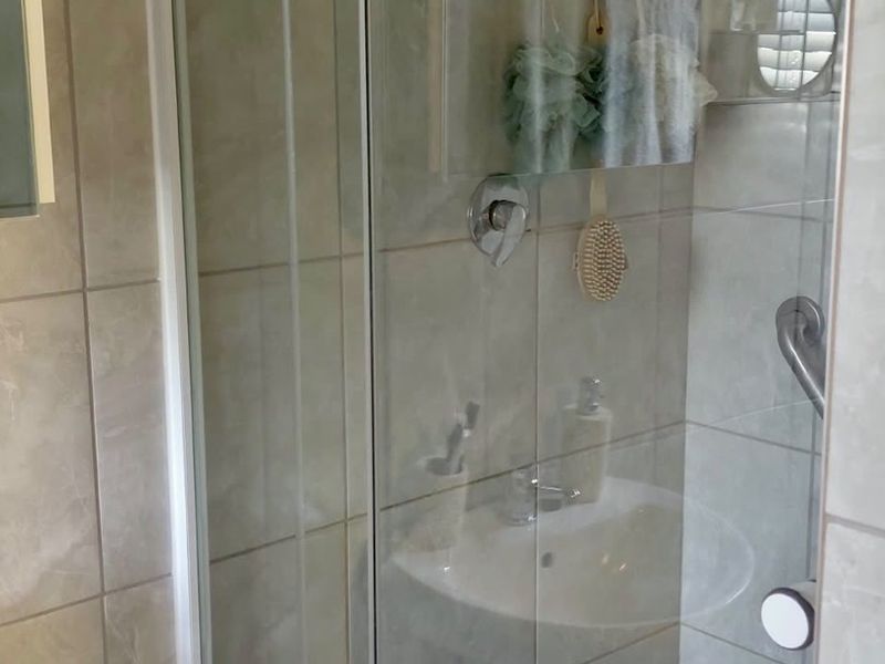 A functional bathroom featuring a glass-enclosed shower and a wall-mounted basin with neutral ceramic tiling.