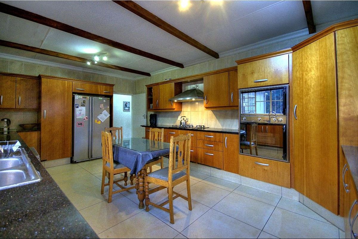 Spacious kitchen featuring wooden cabinetry, granite countertops, built-in oven, gas hob, extractor fan, and tiled flooring with exposed ceiling beams.