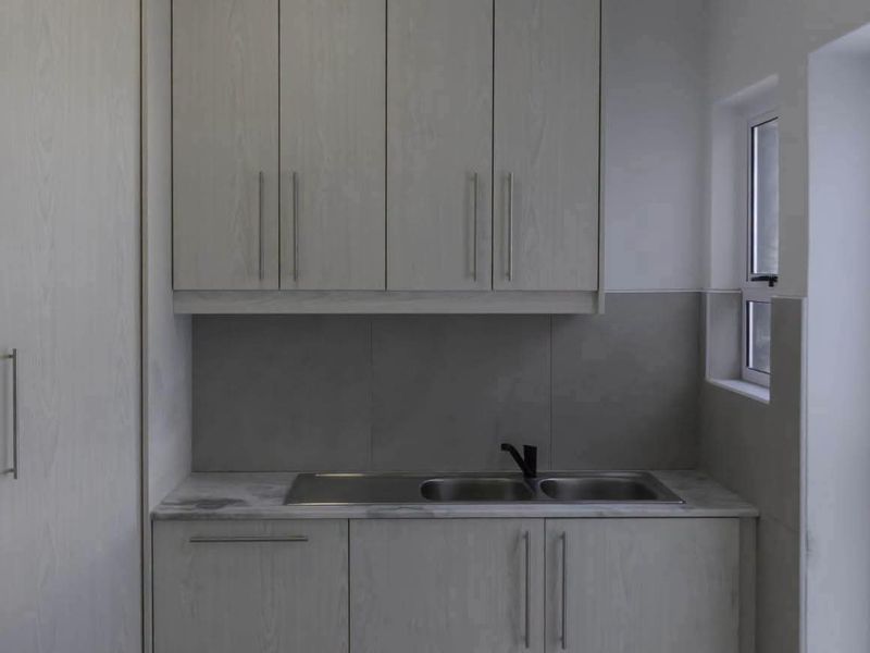 A clean and modern laundry area featuring light wood-grain cabinetry, a stainless steel double sink, and a neutral tiled splashback.