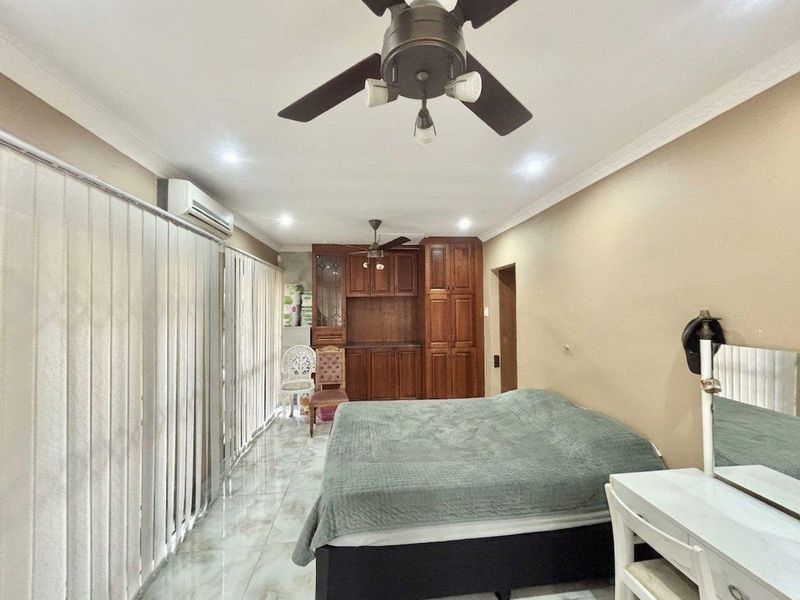 Spacious bedroom featuring tiled flooring, built-in wooden cabinetry, a ceiling fan, and a wall-mounted air conditioning unit.