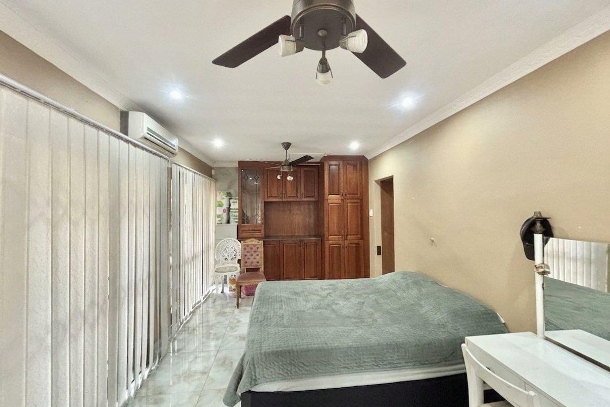 Spacious bedroom featuring tiled flooring, built-in wooden cabinetry, a ceiling fan, and a wall-mounted air conditioning unit.