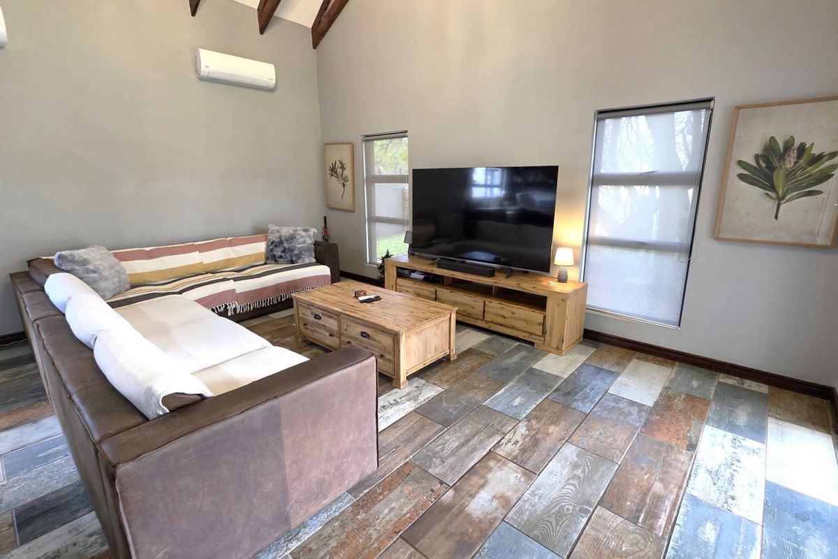 A well-maintained living room featuring vaulted ceilings with exposed timber beams, tiled flooring, and a split-system air conditioner.