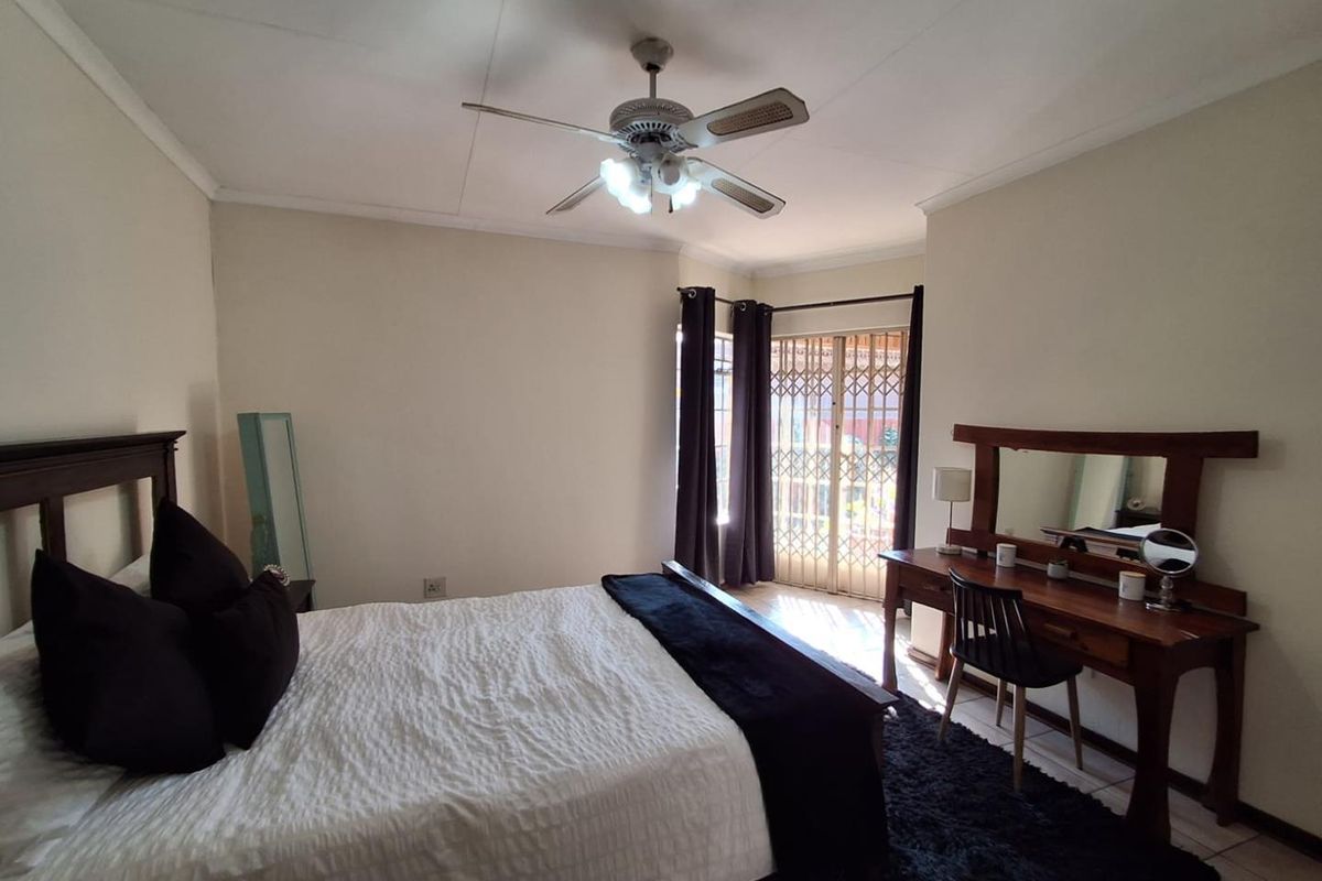 A well-lit bedroom featuring a ceiling fan and a sliding door with security gate leading to an outdoor area.