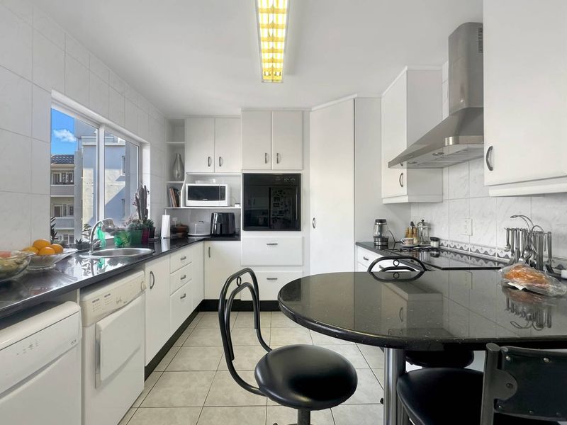 A functional kitchen featuring white cabinetry, black granite countertops, a built-in oven, stainless steel extractor fan, and tiled flooring with a breakfast nook area.