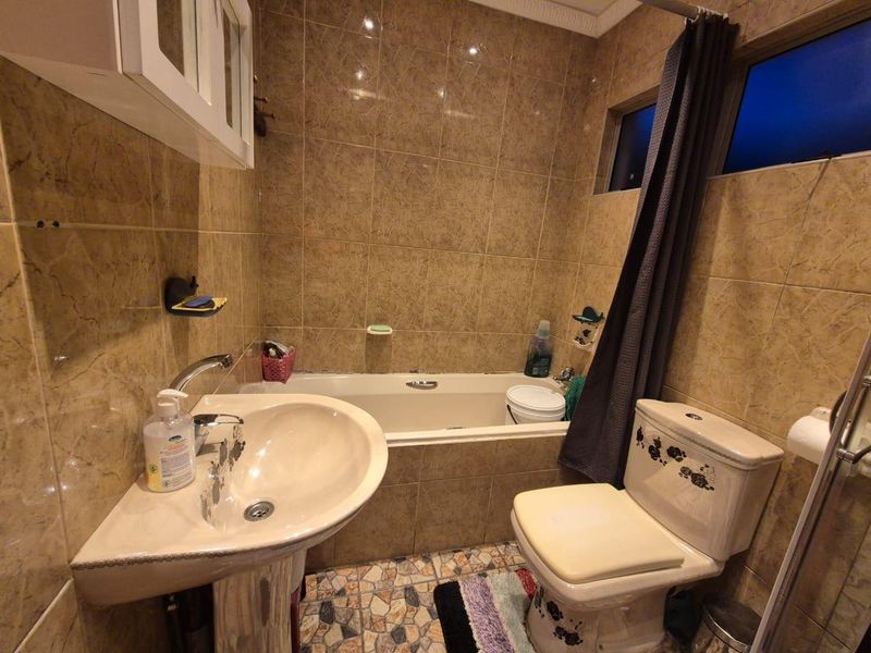 A functional bathroom featuring a pedestal basin, built-in bathtub, and toilet with full-height wall tiling and patterned floor tiles.